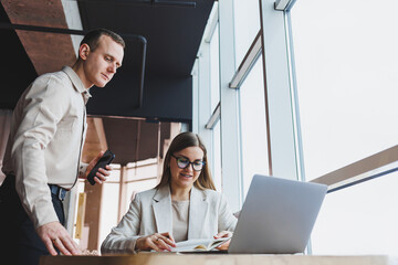 Two different businessmen talking and working together on a new project on a laptop while sitting in a large modern office