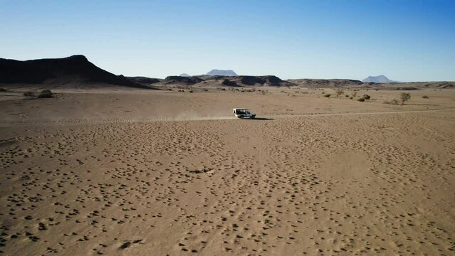 Truck driving on dusty desert track, sandy terrain; low angle drone tracking