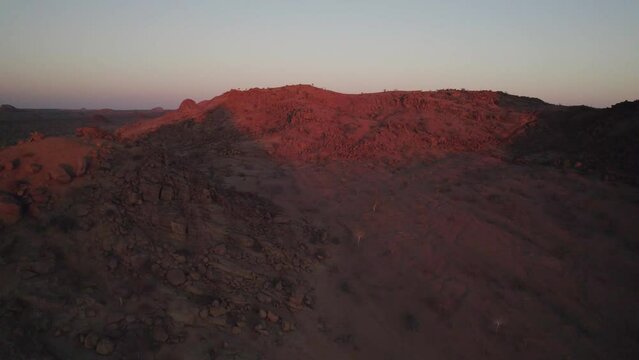 Arid African desert landscape glows red at sunset, Namibia; aerial riser