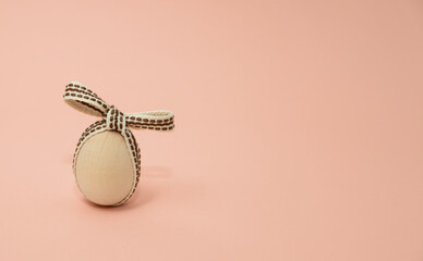 Wooden egg with a bow on a coral background. Easter concept. Copy space.