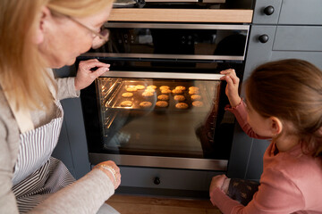 Caucasian grandmother and granddaughter checking the cookies in oven