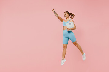 Fototapeta na wymiar Full body young sporty fitness trainer instructor woman wear blue tracksuit spend time in home gym hold scales do winner gesture isolated on pastel plain light pink background. Workout sport concept.