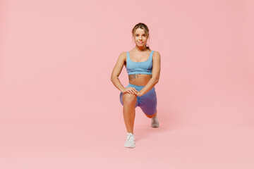 Full length young sporty athletic fitness trainer woman wear blue tracksuit spend time in home gym train do stretch legs squat exercise isolated on plain light pink background. Workout sport concept. - obrazy, fototapety, plakaty