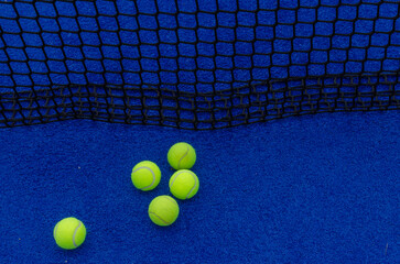 Five paddle tennis balls near the net on a blue paddle tennis court, racket sports