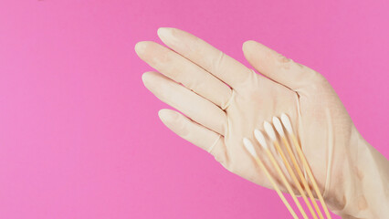 Cotton sticks for swab test in hand palm with white medical gloves or latex glove on pink background.