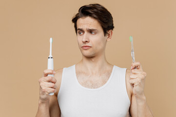 Attractive puzzled minded young man 20s perfect skin wear undershirt hold choice electric brushes...