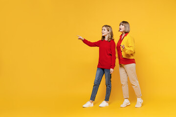 Full body woman 50s in red shirt have fun with teenager girl 12-13 years old. Grandmother granddaughter point index finger aside on copy space area isolated on plain yellow background. Family concept.