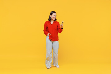 Fototapeta na wymiar Full size body length vivid marvelous magnificent young woman of Asian ethnicity 20s years oldin casual clothes hold in hand use mobile cell phone isolated on plain yellow background studio portrait.