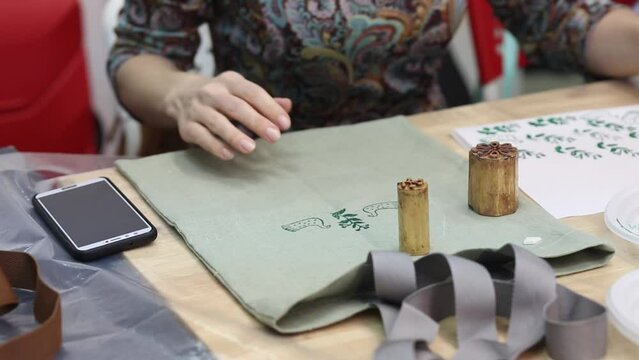 Hand-printed pattern on fabric. Women's hands put a seal on the shopping bag. Ancient traditions. Modern hobbies and creativity.