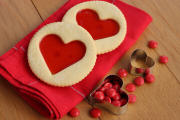 Homemade heart-shapes, cookies with strawberries jam on red place mat on wooden table. Valentine’s day food