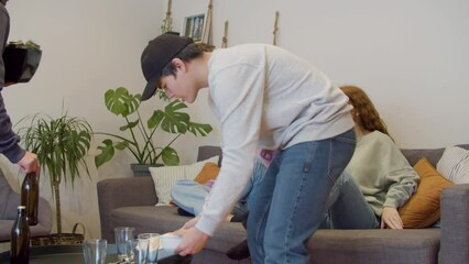 Men bringing food and drinks while women sitting on sofa at home. Happy and excited friends preparing to watch sports games on TV, getting together on weekend and talking. Party, television concept