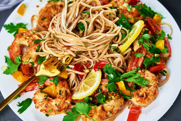 Stir fry noodle with shrimps, lemon and fresh parsley on white plate, soba with prawns, asian cuisine, top view