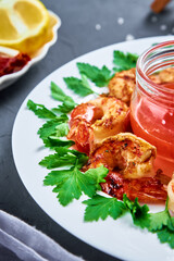 Grilled shrimps on white plate with fresh parsley, spices and lemon, fried prawns with sauce in jar