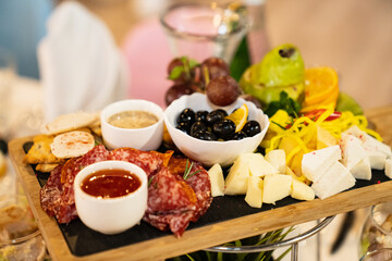wooden tray with appetizers, fruits and sauces. sausage, cheese, olives, grapes, pear, tomato and mayonnaise sauce for the buffet. Catering.