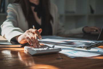 Fototapeta premium Close up of business asian woman or accountant hand holding pen working on calculator to calculate business data, accountancy document and laptop computer at office, business concept