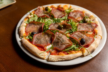 Arugula prosciutto pizza served on white plate