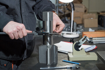The master measures a metal part with a caliper at the factory