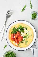Breakfast fried eggs. Rustic omelette or frittatas with green onions, cheese mozzarella, green arugula and tomatoes on light stone background. Healthy food concept. Copy space. Top view. Mock up.