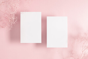 White paper empty blank, dry flowers, dried twig on pink background. Invitation card mockup on beige table. Flat lay, top view, copy space, mockup