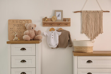 Wooden shelf with baby clothes, toys and furniture in room. Interior design