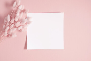White paper empty blank, dry flowers, dried twig on pink background. Invitation card mockup on beige table. Flat lay, top view, copy space, mockup