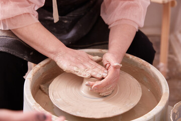 Women's hands create dishes on a potter's electric wheel.