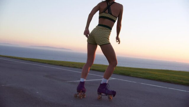 Idyllic natural summer landscape with beautiful sunset skyline and ocean view. Beautiful and healthy woman riding roller skates in the park within seascape. High quality 4k footage