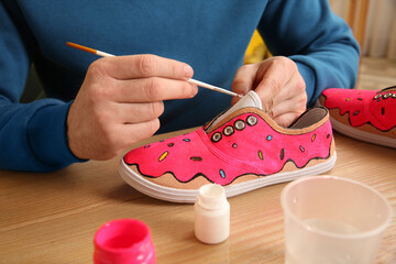 Man painting on sneaker at wooden table indoors, closeup. Customized shoes