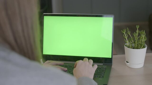 A shot over the shoulder of a business woman typing on a keyboard and looking at a green screen. An office employee using a laptop with a green screen. remote work or training.