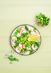 Spring salad plate with radish, cucumber, green pea, sunflower, soy and mung bean sprouts, edamame and flax seeds. Vegetarian vegan healthy food. Top view, green kitchen table