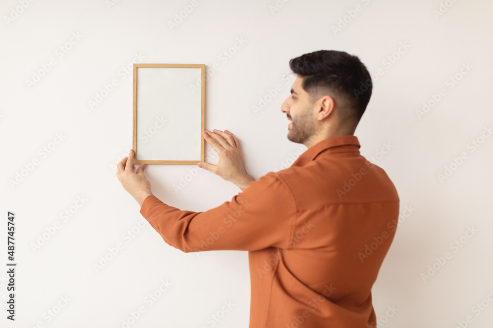 Wall mural Young man hanging picture frame on the wall