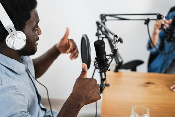 Multiracial hosts streaming podcast together at home studio - Focus on african man headphones