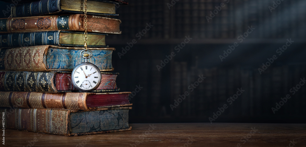 Wall mural old clock hanging on a chain on the background of old books. сlock as a symbol of time a books are a