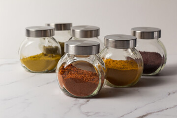 A set of spices for cooking Asian dishes. Ground spices in transparent glass jars on a light background.
Colored ground spices