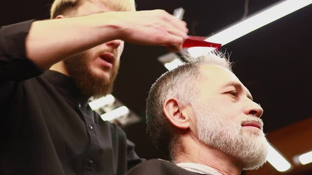 trendy stylish master cuts hair of old man client in modern barbershop