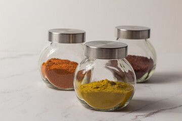A set of spices for cooking Asian dishes. Ground spices in transparent glass jars on a light background.
Colored ground spices