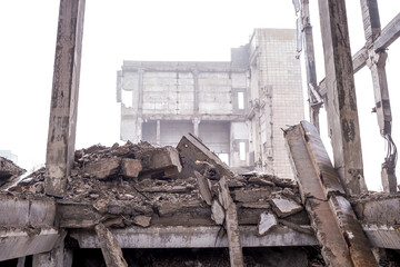 Large concrete beams, piles, slabs and construction debris against the background of the remains of a destroyed building in a hazy haze. Background