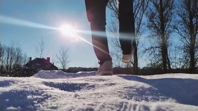Close-up of man funny slipping on ice on winter sunny day outdoors, back view. Male feet slide on snowy road, low angle view, slow motion