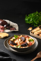 Asturiana fabada with chorizo, bacon, sausage, haricot served fresh crispy toast on black table. Vertical orientation. Tasty traditional spanish warming dinner.