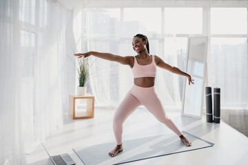 Fit young African American lady practicing yoga, doing domestic fitness, foillowing online video at home gym
