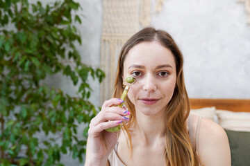 Fototapeta premium Young woman is doing Gua Sha facial massage in bathroom. Gua Sha jade stone at home treatment
