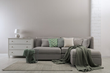 Fototapeta na wymiar Large grey sofa and chest of drawers near light wall in room. Interior design