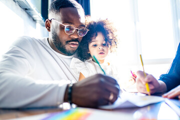 father wearing glasses and adorable little daughter drawing colorful pencils spending leisure time...