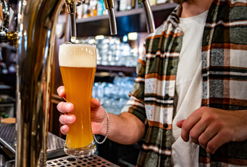 bartender hand at beer tap pouring a draught beer in glass serving in a bar or pub