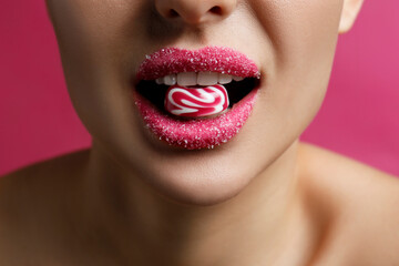 Obraz premium Woman with lips covered in sugar eating candy on pink background, closeup