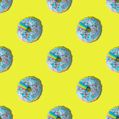 A repeating pattern of blue donuts with a rainbow on a yellow background. Flat lay