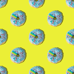 A repeating pattern of blue donuts with a rainbow on a yellow background. Flat lay