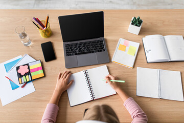 Blonde european teenage girl study at home with computer with blank screen at table in minimalist kitchen