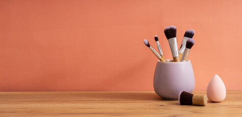 Purple organizer full of makeup brushes,sponge for face on the wooden table against bright orange...