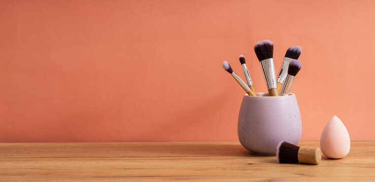 Purple organizer full of makeup brushes,sponge for face on the wooden table against bright orange background.Empty space